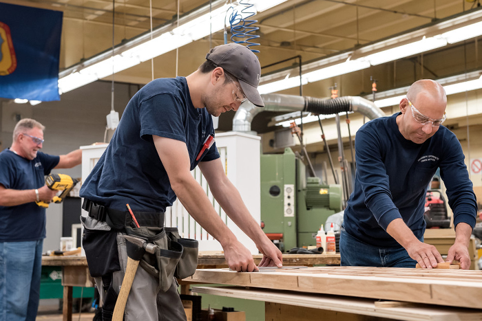 Three people work on building something with wood