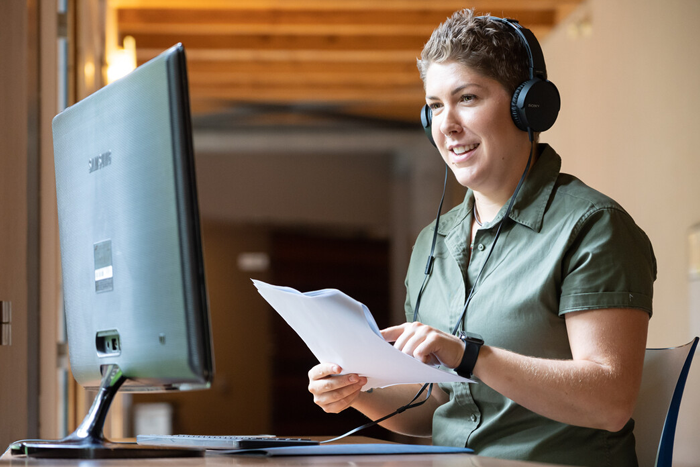 A person sits at a computer with headphones on