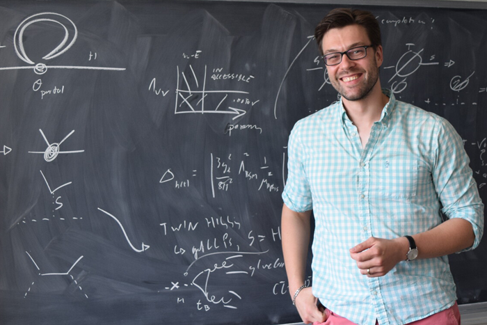 A person stands in front of a chalk board with writing on it