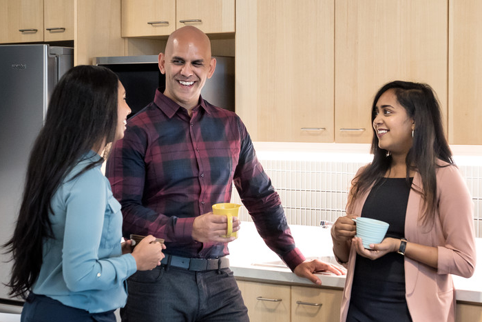 Three people chat in a kitchen holding coffee mugs