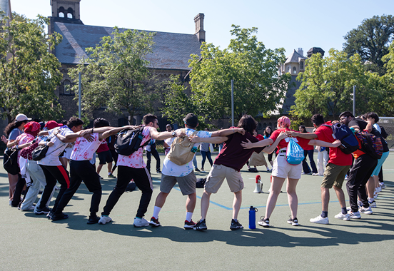 Students stand in a large circle with linked arms at orientation