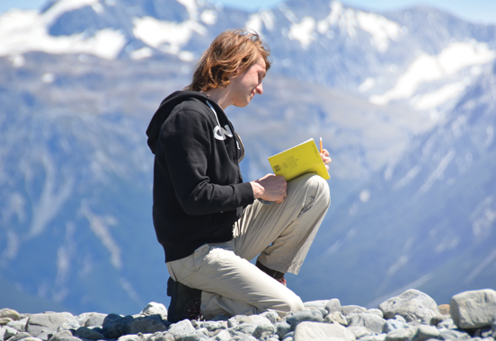 A student kneels on a mountain holding a book