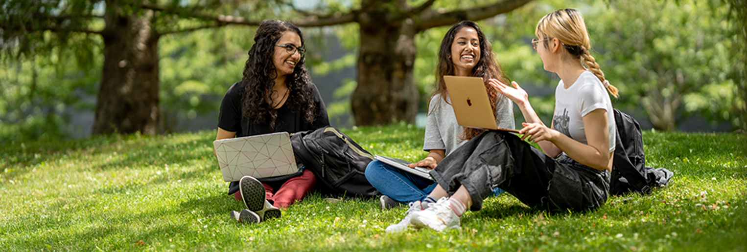 three students sitting on the grass