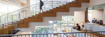 A student walks down a staircase while other students study in the atrium below