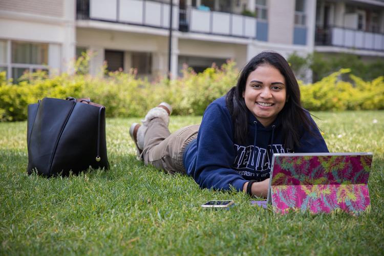 Amanda Khan lies on the grass with her laptop in front of her