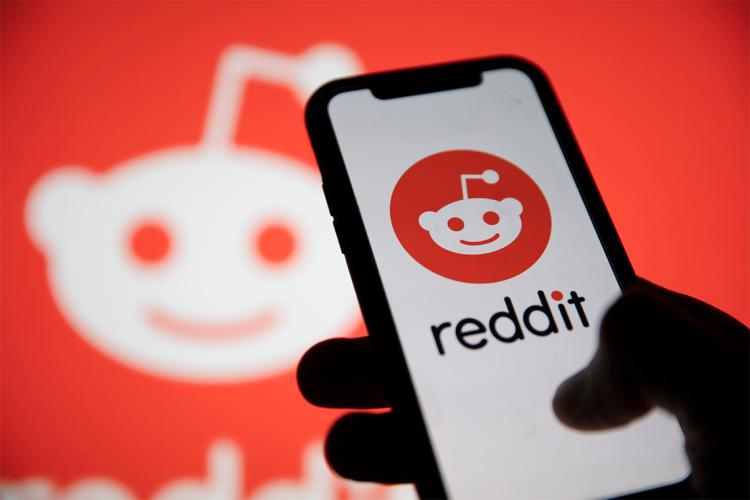 A person hold a cellphone with the reddit logo visible