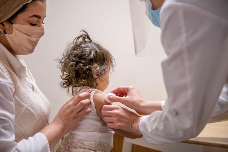 a doctor prepares an infant girl's arm with a cotton swab for a vaccination