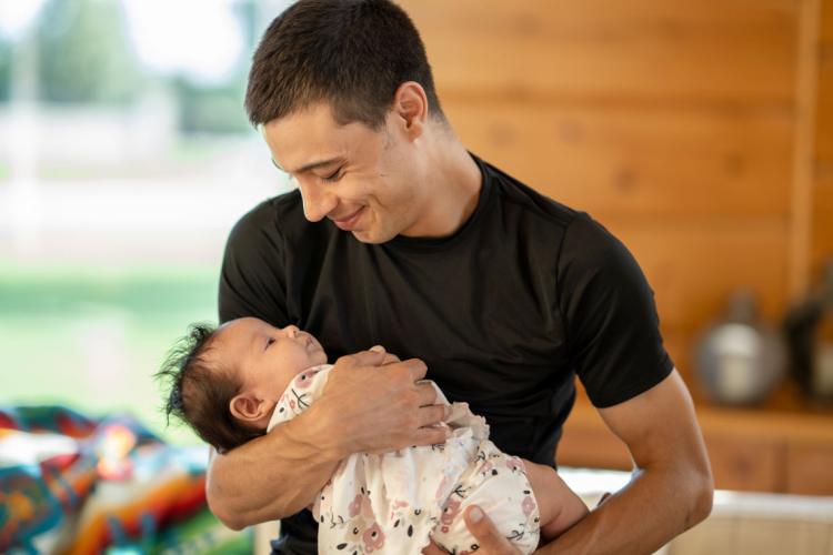 Young Indigenous father holds his infant child in his arms while smiling