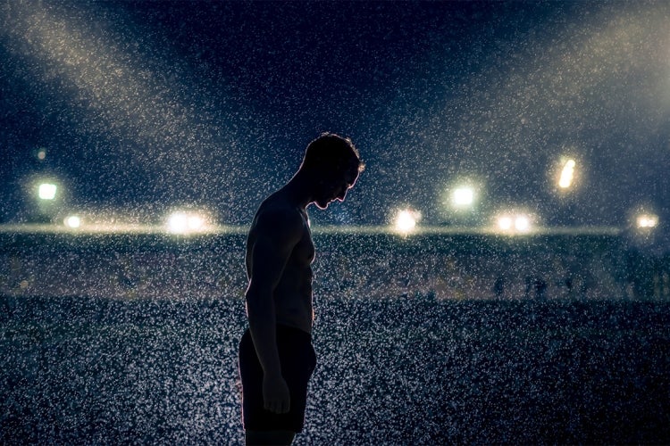 silhouetted athlete looks down at his feet in a darkened stadium