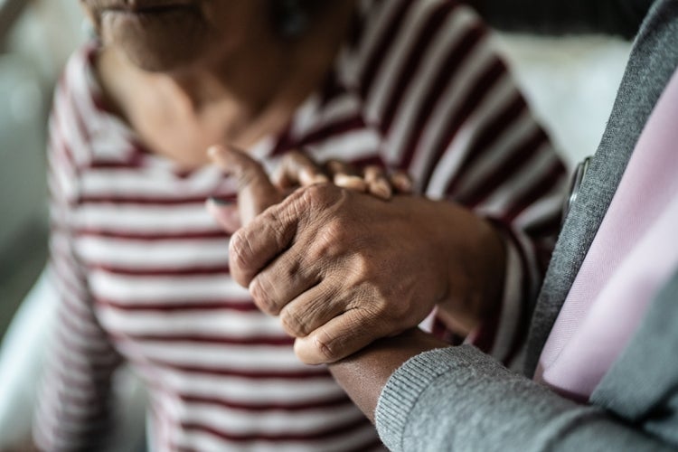 An adult holds the hand of an elderly person