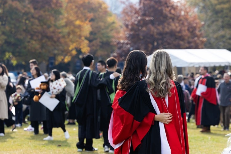 two female graduates are seen from the back as they take a selfie on front campus after their convocation ceremony