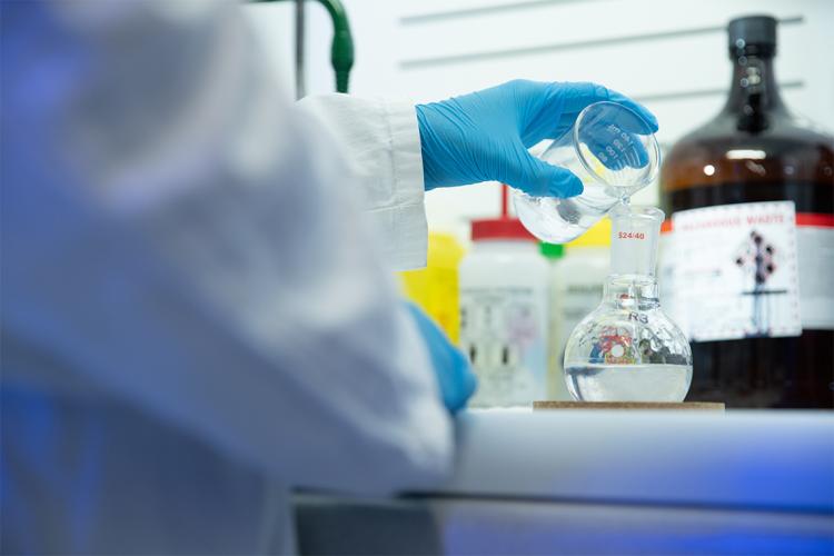 a person pours liquid into an Erlenmeyer flask at Genecis