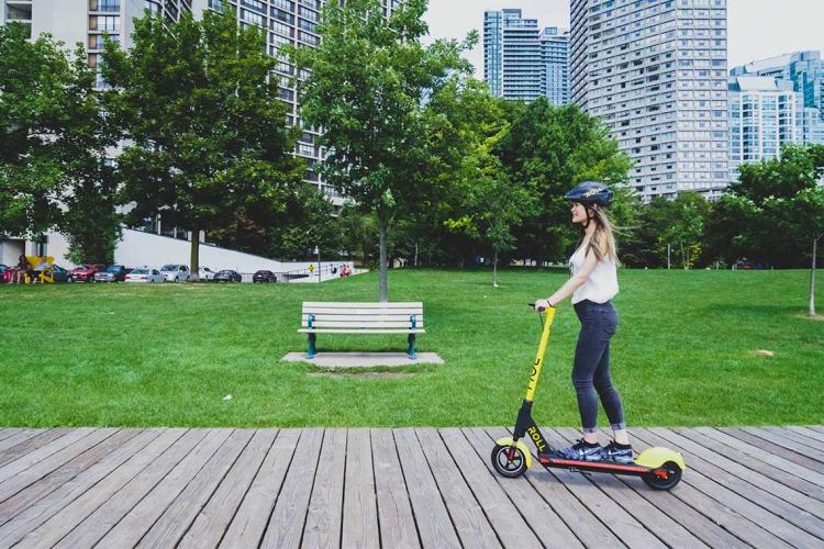 A woman rides a Roll brand e-scooter in Toronto along the boardwalk downtown