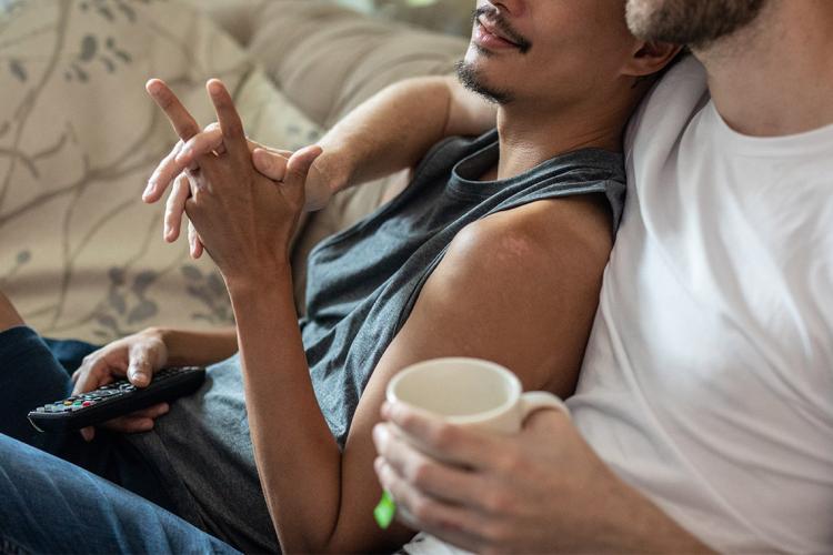 Photo of two men holding hands as they sit on a sofa