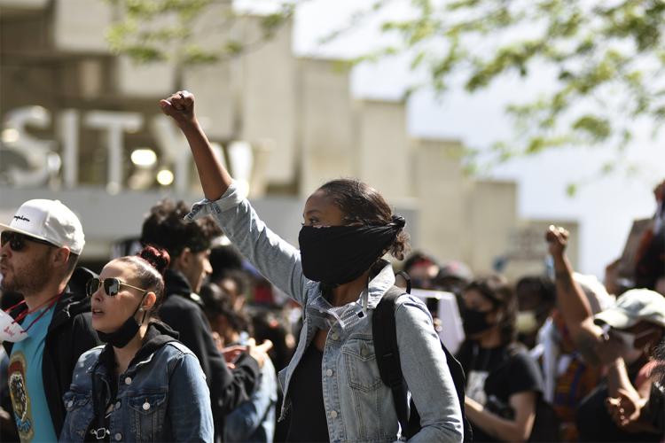 A young Black woman raises her fist in the air at a Black lives matter protest