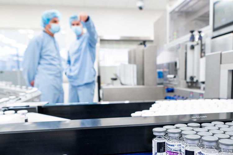 two workers in the background of a vaccine production line