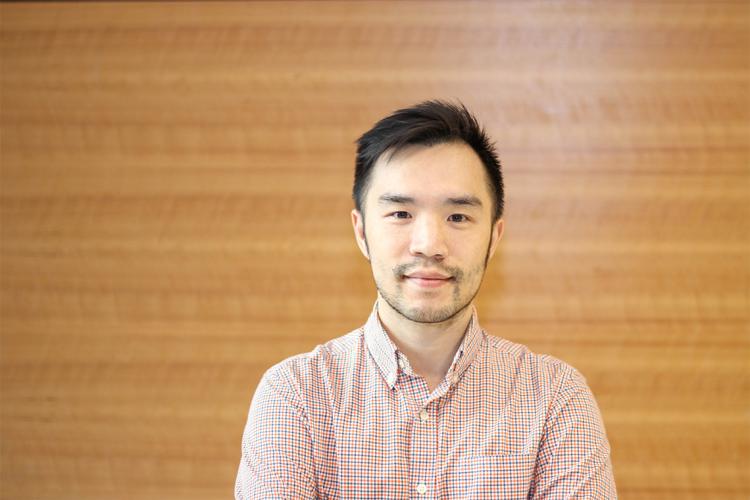 A portrait of Leo Chou standing front of a wooden wall