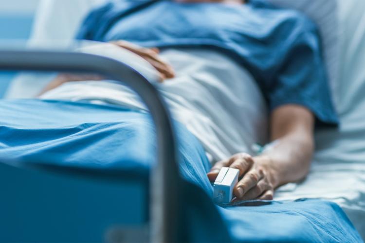 Person lying down in a hospital bed with a monitor on their finger