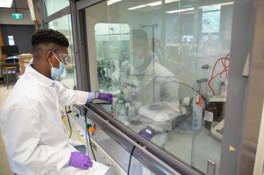 Gaius St. Marie works in a lab using a fume hood behind glass