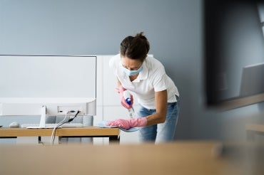 mature woman cleaning an office while wearing a surgical mask