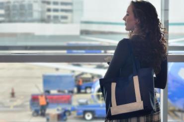 woman standing by a window at the airport carrying an upcycled leather bag made from airplane seats