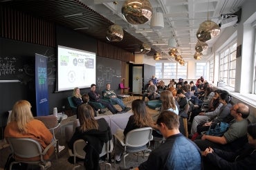 A large group of students sit in a room for the hackathon