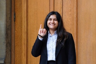 Vishakha Pujari holds up her pinky finger with her engineering ring outside of convocation hall at the University of Toronto