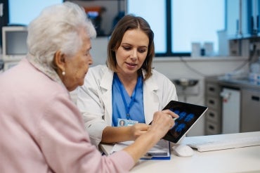 a doctor shows an elderly woman brain scans on an ipad