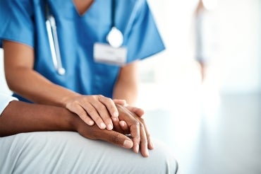 a black doctor holds the hand of a black patient at a hospital