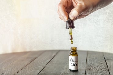 hand with eyedropper that's being pulled out of a small vial of CBD oil