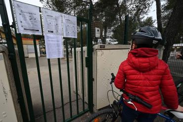 photo of a boy in a red jacket looking at a coronvirus sign hanging on a playground gate