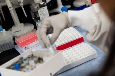 a latex gloved hand of a lab tech handles a vial with coronavirus in it