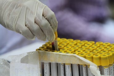 a lab technician handles a vial of blood for a Covid-19 antibody test