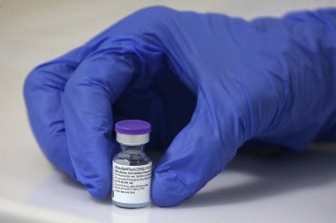 A gloved hand holds a vial of pfizer covid vaccine