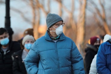 older man walks down the street wearing an n95 respirator while those around wear cloth and surgical masks