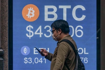 a man walks past a digital sign showing values for bitcoin and etherium cryptocurrency