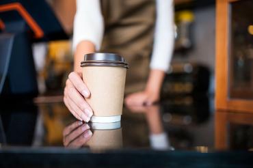 a coffee shop employee giving someone a takeout cup of coffee