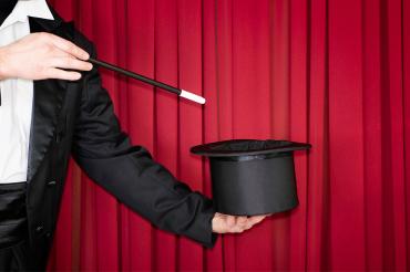 a magician points their wand at a top hat while on stage