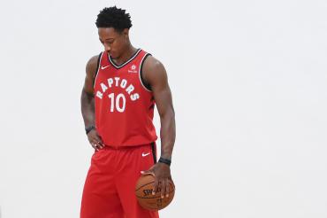 DeMar DeRozan, in a red Raptors uniform, holds a basketball at his side