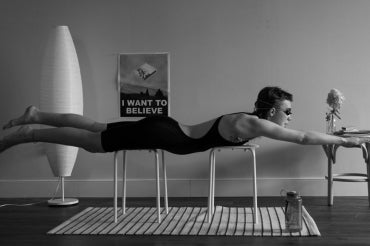 Person in a living room set on top of chairs in a horizontal position practicing swimming 