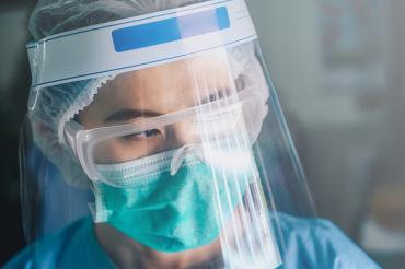 asian female nurse wearing multiple layers of PPE looking serious