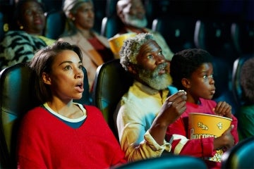 A mother, father and child have a look of surprise on their faces while watching a movie at a theatre