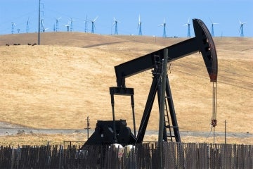 an oil drill in the foreground with a row of wind turbines in the background