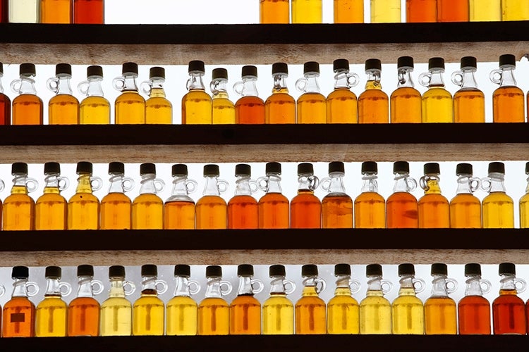 Glass jars of maple syrup sit in front of a window.